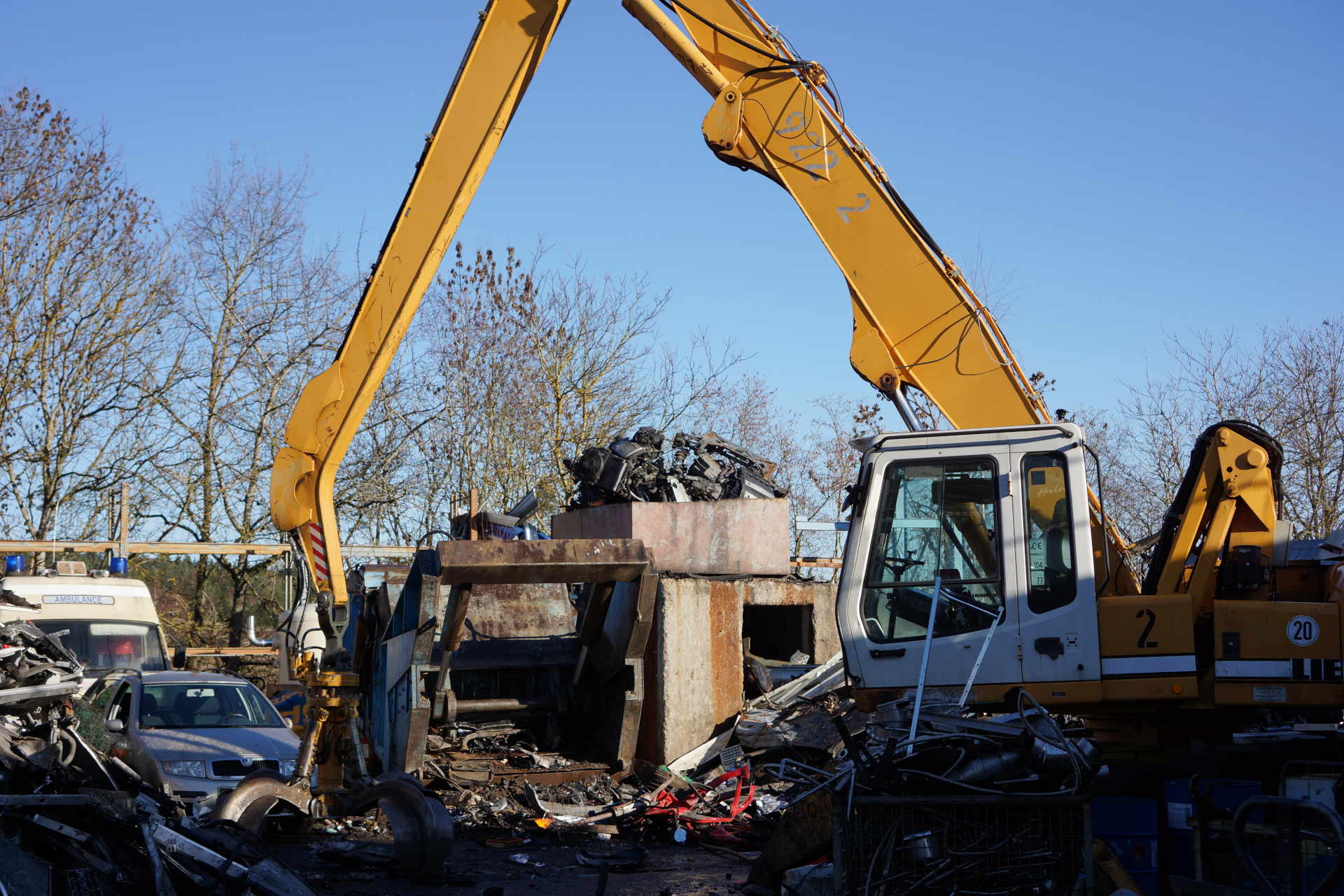 Bagger umgeben von Schrott vor einer Schrottpresse